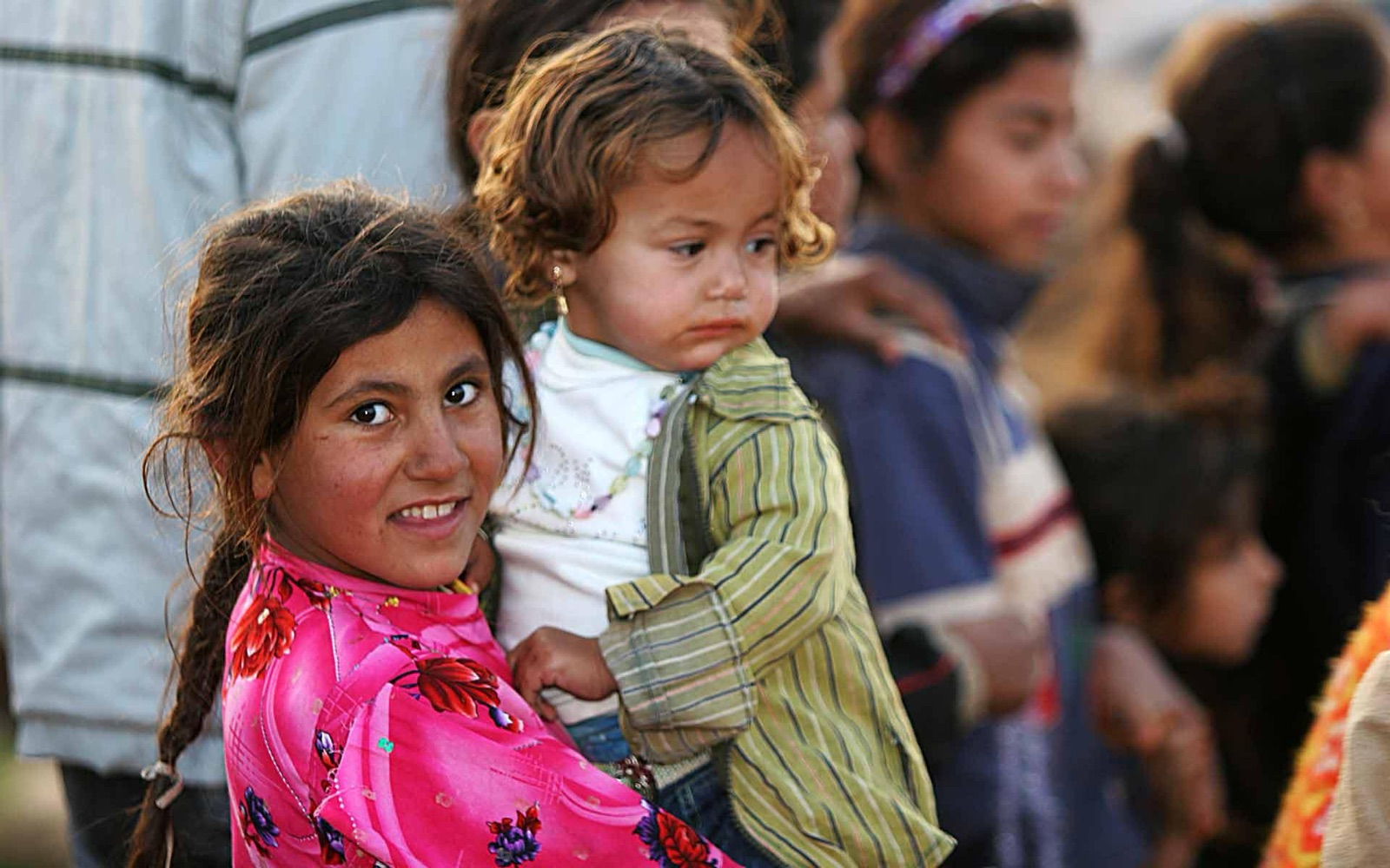 A refugee girl carries her younger sibling through a crowd